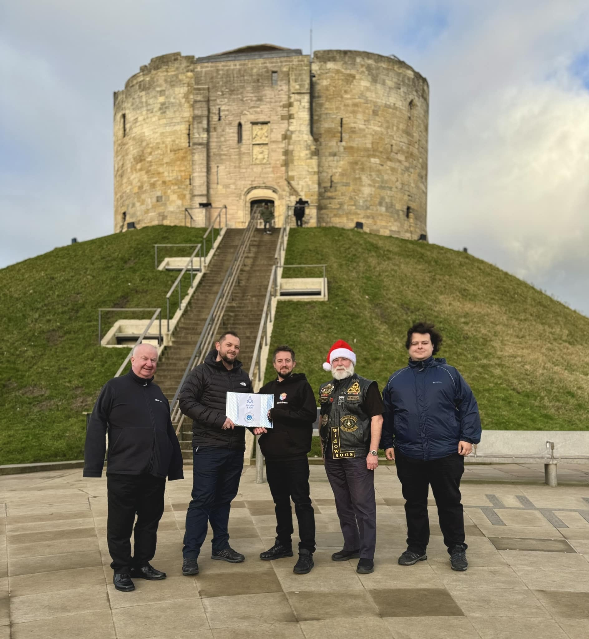 5 men stood in front of a stone tower presenting an letter